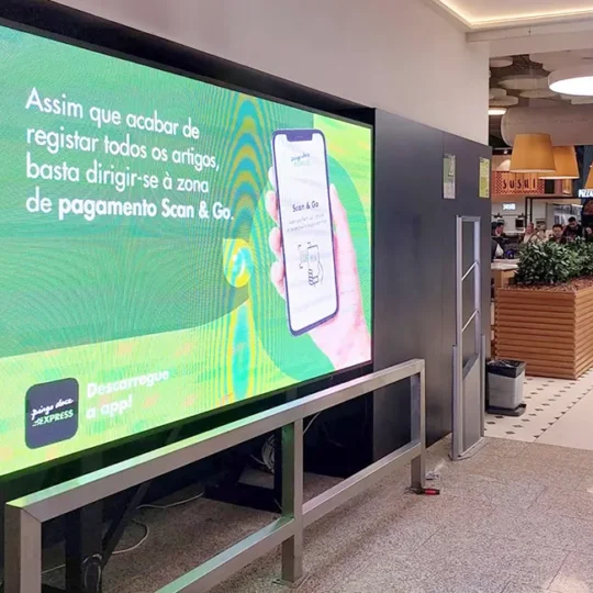 Painel LED para Interior com cerca de 98'', instalado na entrada de hipermercado Pingo Doce a reproduzir conteúdos em fundo verde, promovendo a utilização da App.